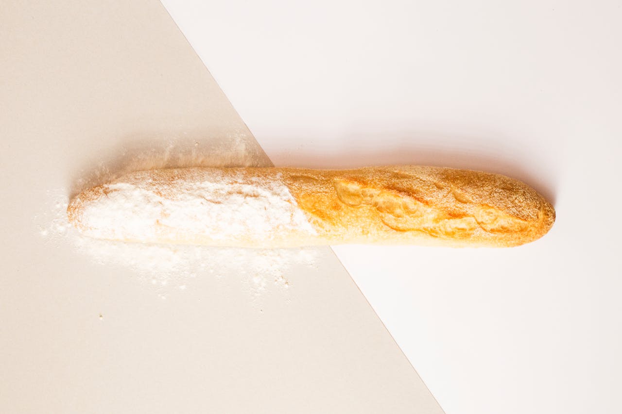 Close-up of a fresh baguette dusted with flour on a minimalist background.